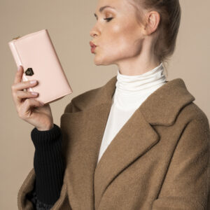 Skórzany portfel damski zamykany na zatrzask w kolorze pudrowego różu, trzymany przez modelkę - Lakierowany portfel damski Betlewski®